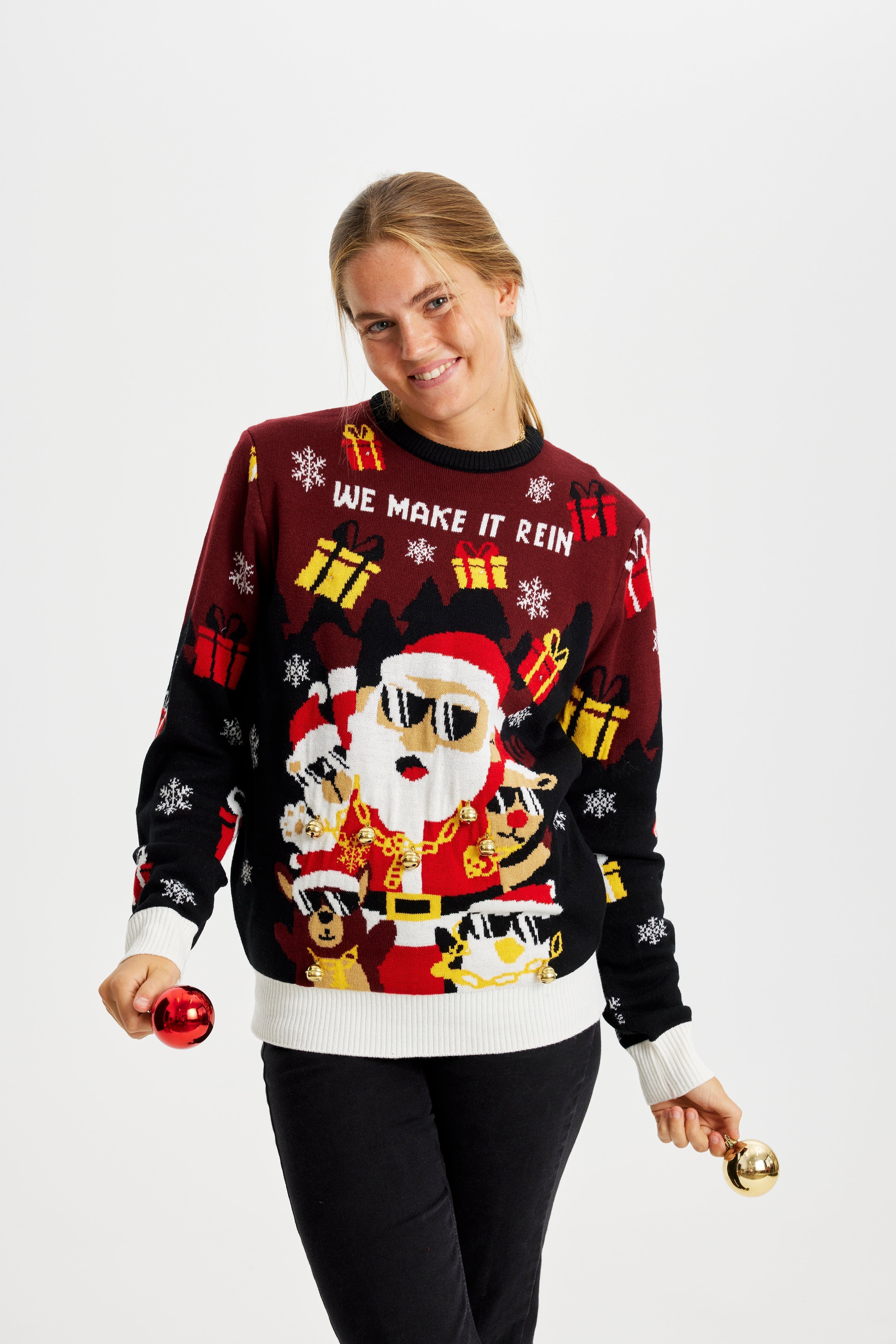 Een lachende vrouw in een rode en zwarte kersttrui met een kerstfiguurtje en cadeautjes.